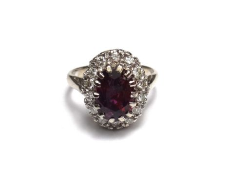 A ruby and diamond set oval cluster ring, claw set with the oval cut ruby at the centre, within a surround of circular cut di