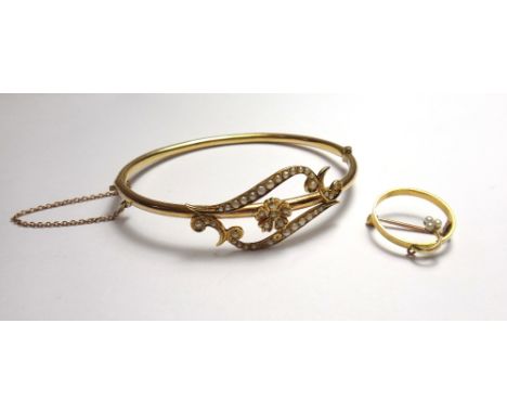 A gold and seed pearl set oval hinged bangle, the front with a central flowerhead motif, between scrolling sides, (three seed