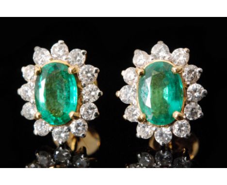 A pair of 18ct emerald and diamond earrings, each with oval cut emerald with a surround of thirteen brilliant cut diamonds ea