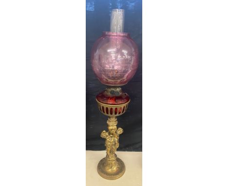 Brass oil lamp, cranberry shade and font with cherubs, approximate height 28 inches