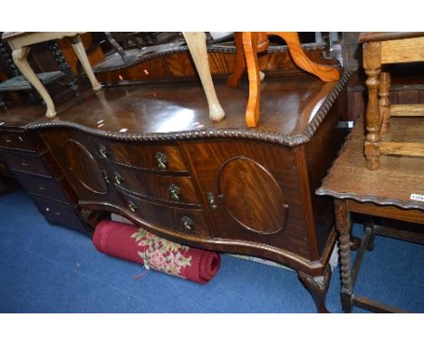 A 20TH CENTURY MAHOGANY SERPENTINE SIDEBOARD, with three central drawers on ball and claw feet (key)