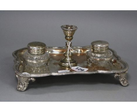 A SILVER PLATED SHAPED RECTANGULAR DESK STAND, fitted with two inkwells and a taper stick, on four acanthus cast feet, width 