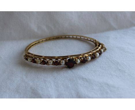 A Garnet and pearl set hinged bangle, with a large oval garnet and eight circular garnets and ten pearls, to a 9ct yellow gol