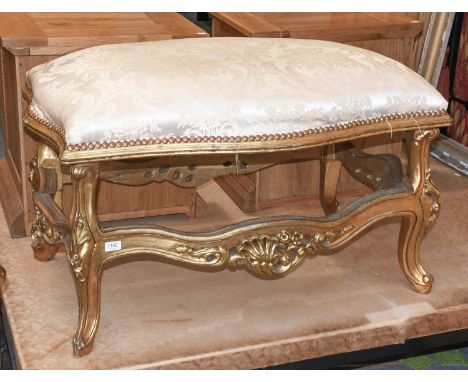 A Louis XV Style Gilt Framed Stool, the shaped padded seat above a framework carved with shells and leaves, 104cm by 62cm by 