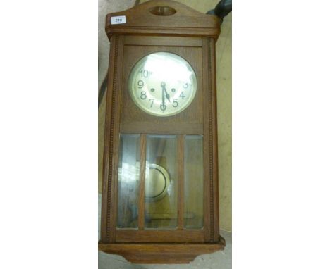 An early 20thC light oak cased wall clock with a bevelled glazed pendulum window; the gong strike movement faced by a silvere