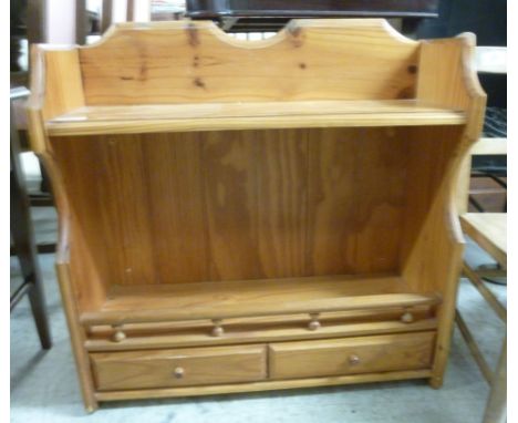 A modern honey coloured pine hanging shelf, having a yoke shaped galleried back, over an open shelf and two in-line drawers, 