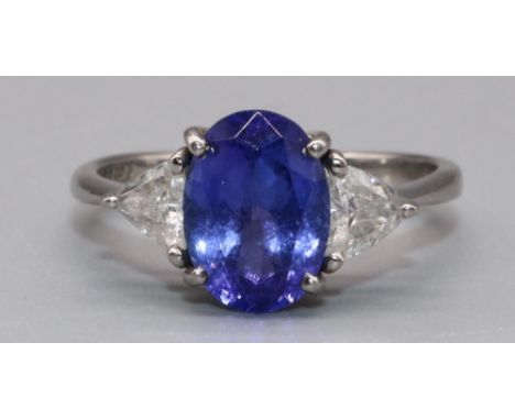 Platinum three stone tanzanite and diamond ring, the central oval cut tanzanite flanked by two triangle cut diamonds in claw 