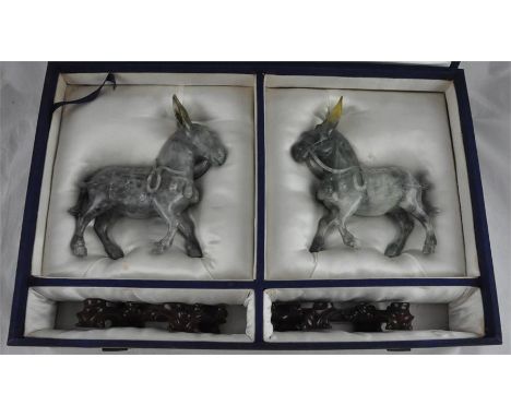 A pair of modern Chinese green/grey jade donkeys on stands, each beast with harness and saddle with calligraphy, in fitted bo
