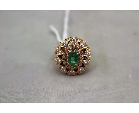 A 14ct. rose gold, diamond and emerald cluster ring,&nbsp;having central oval cut emerald with pierced, deep reverse tapered&