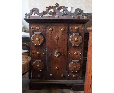 A 17th/18th Century European wooden storage cabinet, brass studded throughout, pierced pediment, single central door, bracket