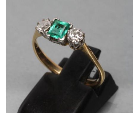 AN EMERALD AND DIAMOND THREE STONE RING, centred by a square cut emerald claw set and flanked by two old cut diamonds to tape