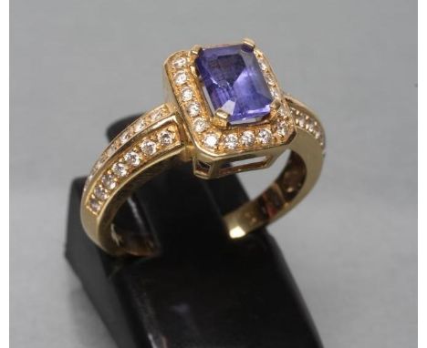 A TANZANITE AND DIAMOND DRESS RING, the oblong facet cut tanzanite claw set to a border of point set small diamonds and simil