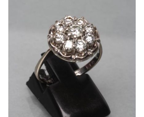 A NINE STONE DIAMOND CLUSTER RING, the round brilliants point and open set to a flower border and a plain white shank stamped