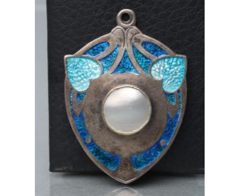 AN EDWARDIAN SILVER AND ENAMEL SECESSIONIST PENDANT, maker James Fenton, Birmingham 1909, the shield panel centred by a mothe