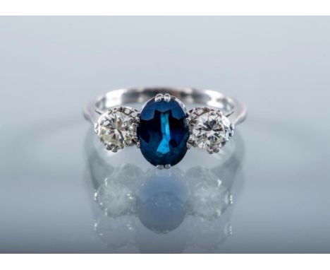 A SAPPHIRE AND DIAMOND THREE STONE RING, the central facet cut oval sapphire claw set and flanked by two brilliant cut diamon