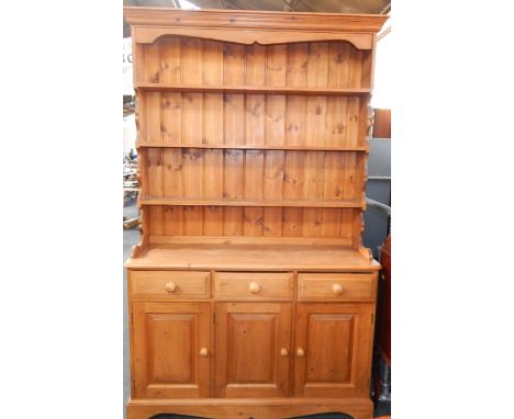 A pine dresser, the outswept pediment above a three shelf delft rack, over three drawers with cupboards below, raised on a br