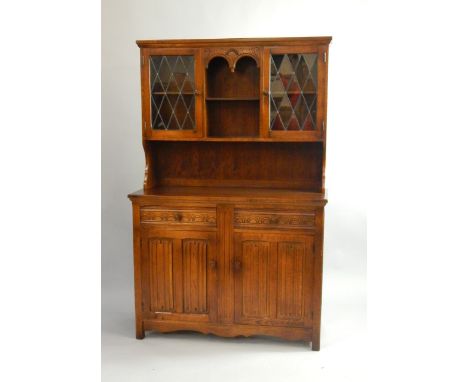 An oak dresser, the top with a recess enclosing a single shelf, flanked by astragal glazed doors enclosing shelves, above two