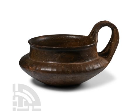 Early 7th century B.C. With burnished deep brown surfaces, the body tapering to a flat foot, the shoulders decorated with ver