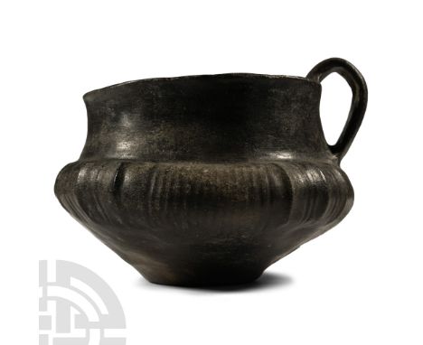 12th-8th century B.C. Squat in profile with low neck and broad mouth, rounded rim, strap handle; carinated shoulder with vert