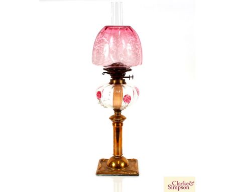 An Art Nouveau brass column table oil lamp, the reservoir with raised pink pruntz decoration, and ruby shade, 67cm high