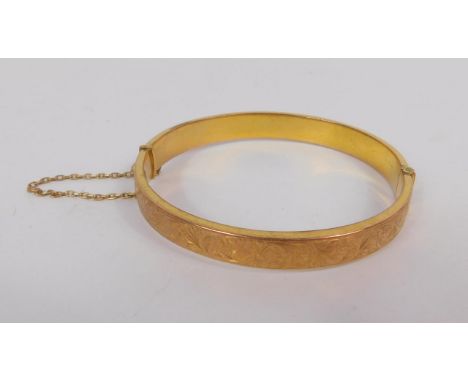 A 9ct gold bangle, foliate engraved, on a snap clasp with safety chain, as fitted, 9.4g.