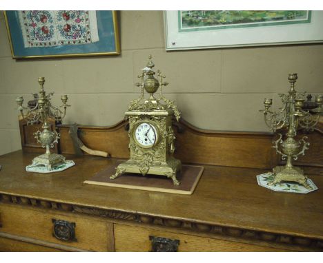 A Continental brass clock garniture, the clock in ornate cast brass case with ivory coloured enamel dial with arabic numerals