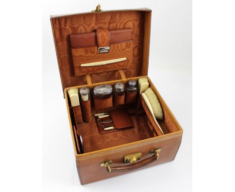 A vintage brown leather vanity case by Finnegan of Manchester fitted with ivory-backed brushes and silver-topped jars dated L