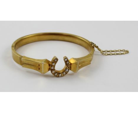 A Victorian yellow metal hinged bangle with central horseshoe motif set with seed pearls (one pearl missing), diameter approx