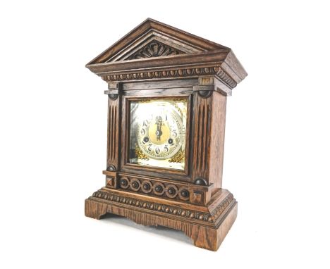 A late 19th/early 20thC German mantel clock, in an architectural carved oak case, the brass dial with rococo scroll spandrels