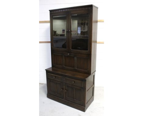 An Ercol 'Old Colonial' style cupboard, two glazed doors with two interior shelves above a drop-down cocktail unit, above two