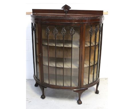 An Edwardian bow-front display cabinet with two interior shelves, carved decorative designs to glazing, raised on small cabri