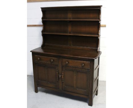 An Ercol 'Old Colonial' style dresser with two plate racks above two frieze drawers, over two panelled cupboard doors, on blo