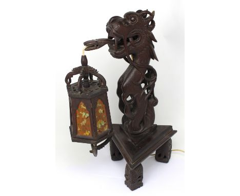 An early 20th century Oriental hardwood lamp in the form of a dragon with serpent tongue suspending octagonal lamp with hand 
