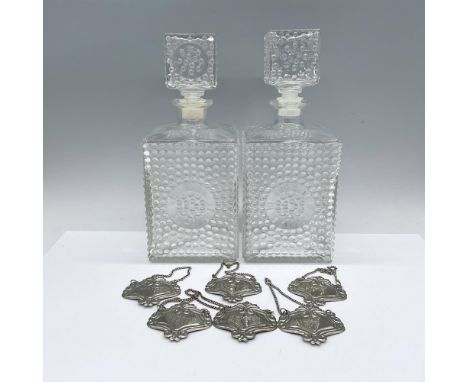 A set of 2 rectangular glass liquor vessels with stoppers each in a hobnail pattern. Includes silvery metal liquor labels. De