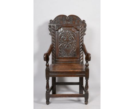 An early 18c oak open armchair with down swept arms, having solid panelled seat, the back panel profusely carved with a centr