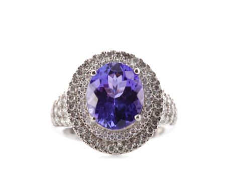 TANZANITE AND DIAMOND RING, set with an oval tanzanite of approximately 5.35 carats, within a double halo of round brilliant 