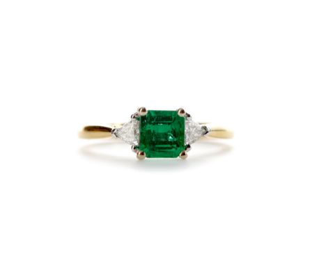 EMERALD AND DIAMOND RING, set with a step cut emerald of approximately 0.76 carats flanked by two trillion cut diamonds total