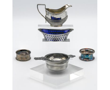 A small silver cream jug, two silver napkin rings, silver and pierced mustard dish with blue glass liner, tea strainer and st