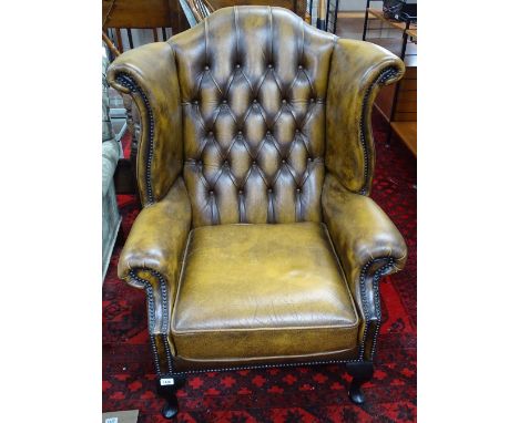 A brown button-back upholstered wing fireside armchair, cabriole legs