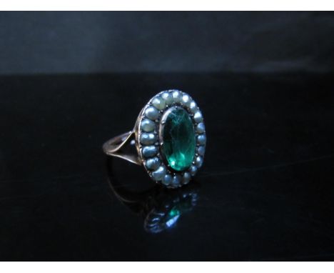 A Georgian gold closed back ring set with central emerald green oval paste stone, framed by grey pearls in basket mount, open