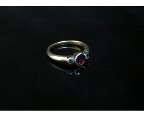 A 9ct gold ruby and diamond ring the central circular ruby flanked by diamonds in rubover setting. Size K, 2.3g 