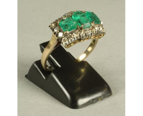 AN EMERALD AND DIAMOND RING, the central facet cut oblong emerald flanked by a pair of square cut stones to a shaped border o