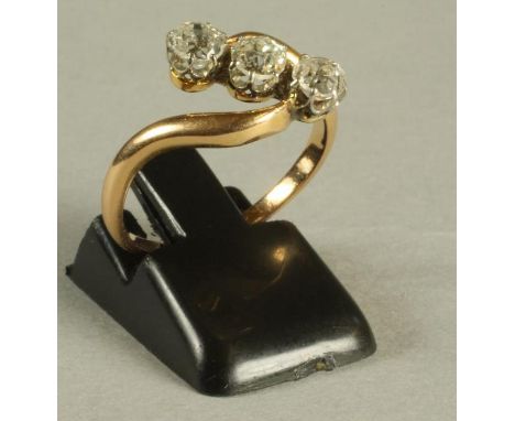 A VICTORIAN THREE STONE DIAMOND RING, the old brilliant cut stones claw set in a crossover setting to a plain gold shank, siz