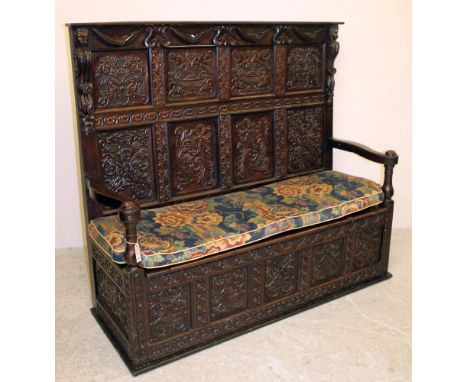 A VICTORIAN CARVED OAK PANELLED SETTLE, the back featuring urns and foliate scrolls, straight top rail on mask corbels over f