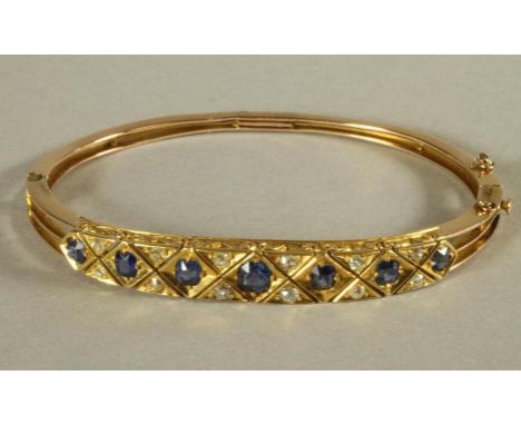 A VICTORIAN SAPPHIRE AND DIAMOND SET STIFF HINGED BANGLE, the cross hatched upper section gypsy set with seven facet cut sapp