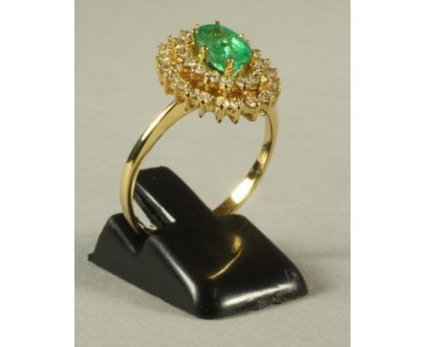 AN EMERALD AND DIAMOND CLUSTER RING, the central oval facet cut emerald claw set to two open borders each similarly set with 