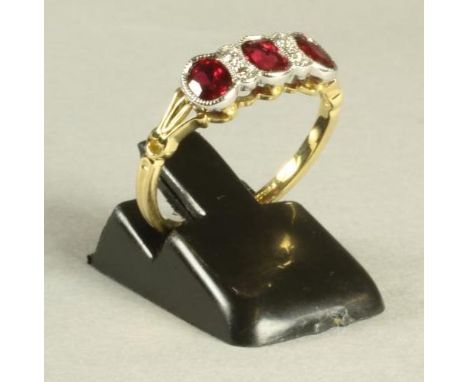 A BURMESE RUBY AND DIAMOND RING, the three oval facet cut rubies open back collet set in white gold and interspersed with two