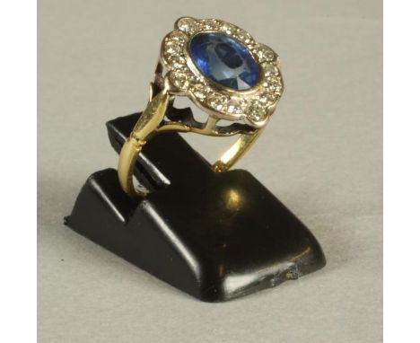 A SAPPHIRE AND DIAMOND CLUSTER RING, the oval facet cut sapphire open back collet set to a border of twelve small diamonds wi