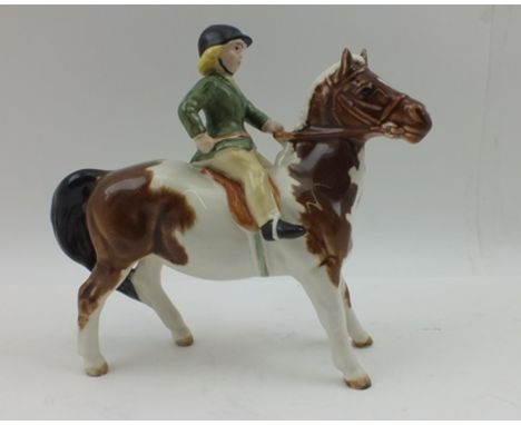 A BESWICK CERAMIC FIGURINE of a girl riding a skewbald pony, no. 1499, she wearing a green hacking jacket, 14cm high 