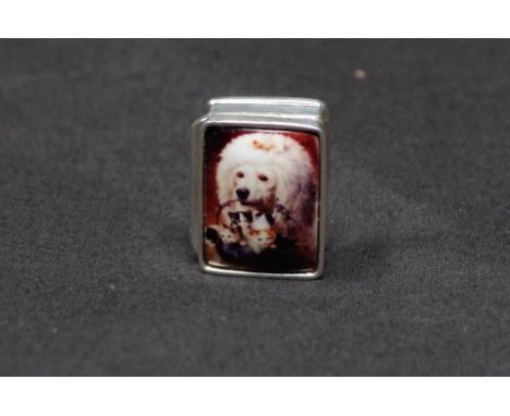 A silver pill box with enamel plaque inset to the lid depicting a French poodle carrying a basket of kittens. Stamped Sterlin